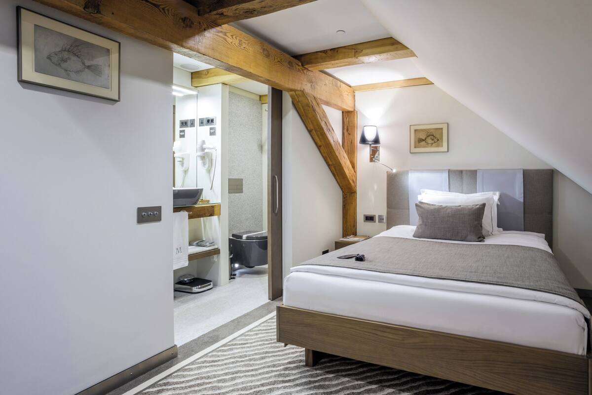 A bedroom with a wooden ceiling, a bed with white bedding, a nightstand, and a headboard.