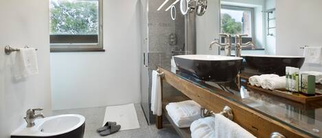 A modern bathroom with a glass shower enclosure, a freestanding bathtub, a large vanity with a black sink, and a mirror above the sink.