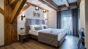 Quarto com teto de madeira, cama com roupa de cama branca, mesa de cabeceira e criado-mudo.