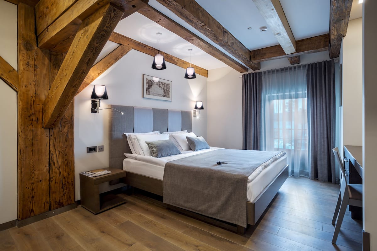 A bedroom with a wooden ceiling, a bed with white linens, a bedside table, and a nightstand.