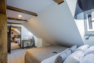 Quarto com teto inclinado, uma cama, uma escrivaninha e uma cadeira.