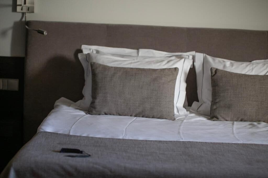 A neatly made bed with white linens and two grey pillows.
