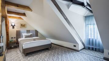 Un dormitorio con techo inclinado, cama, mesita de noche, lámpara y ventana con cortinas.