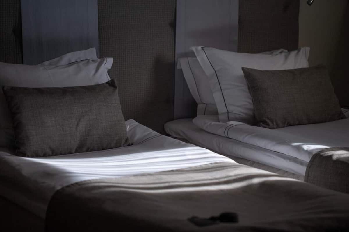 A hotel room with two single beds, each with a pillow and a blanket.