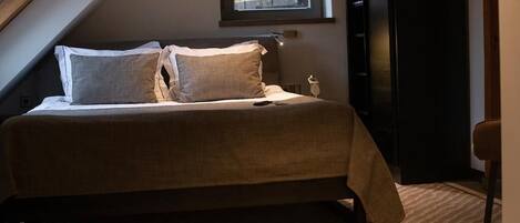 A bedroom with a bed, pillows, a bedside table, a lamp, and a window.