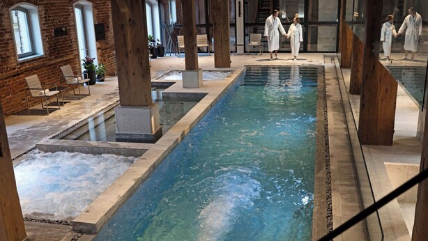 Uma área de spa com uma grande piscina interior, assentos e pilares de madeira.