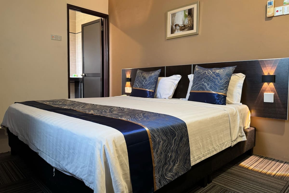 A hotel room with a large bed, a nightstand, a wall-mounted light, and a door.