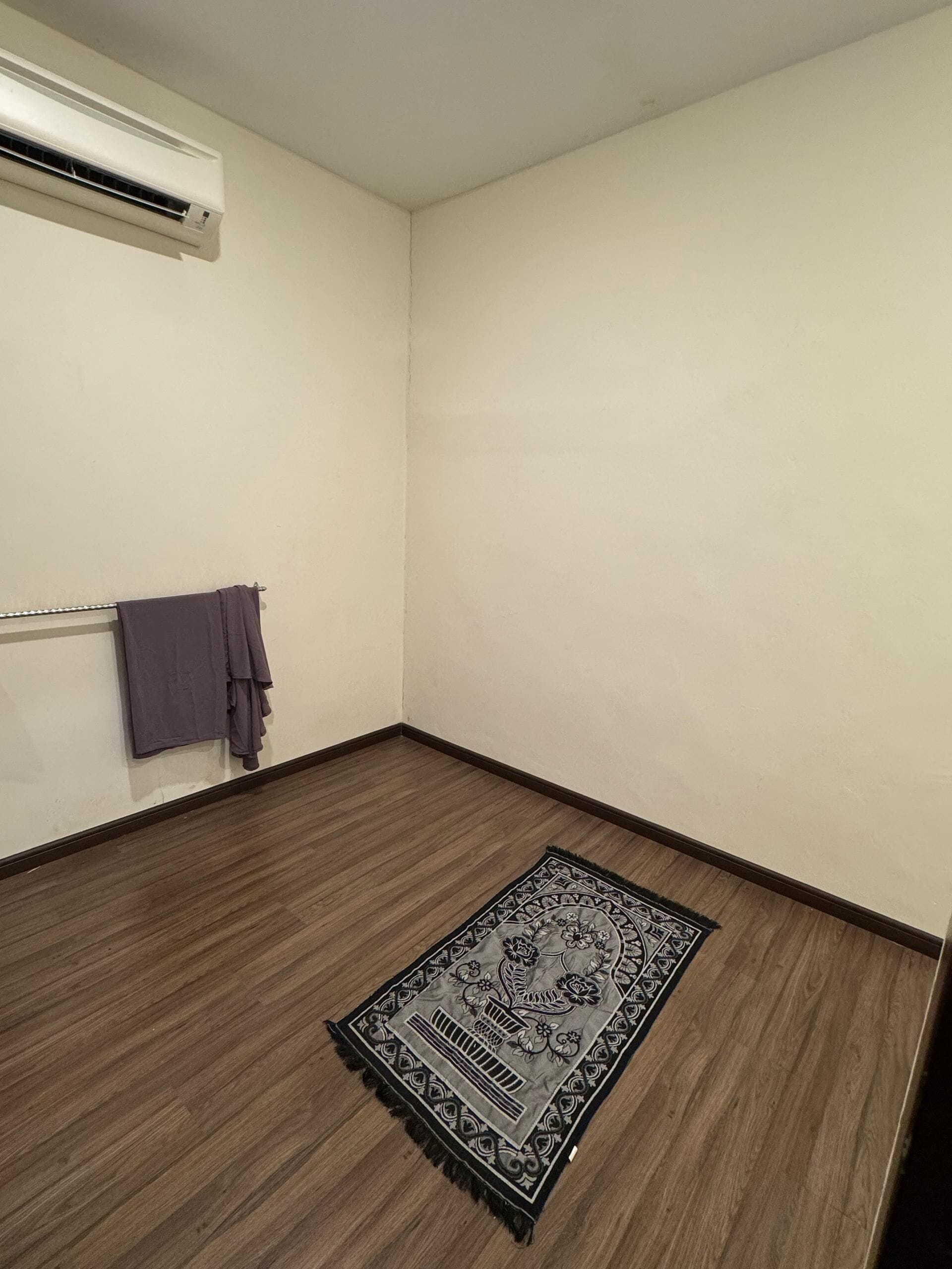 A room with a wooden floor, a patterned rug, a towel on a rack, and an air conditioning unit on the wall.
