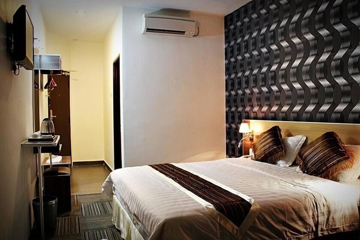A hotel room with a bed, bedside table, lamp, and a patterned wall.