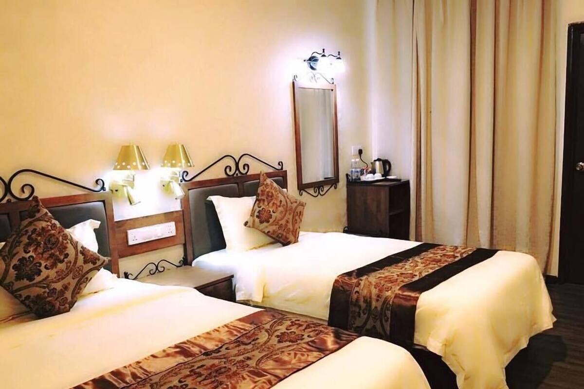 A hotel room with two beds, a bedside table with lamps, a mirror, and a door.