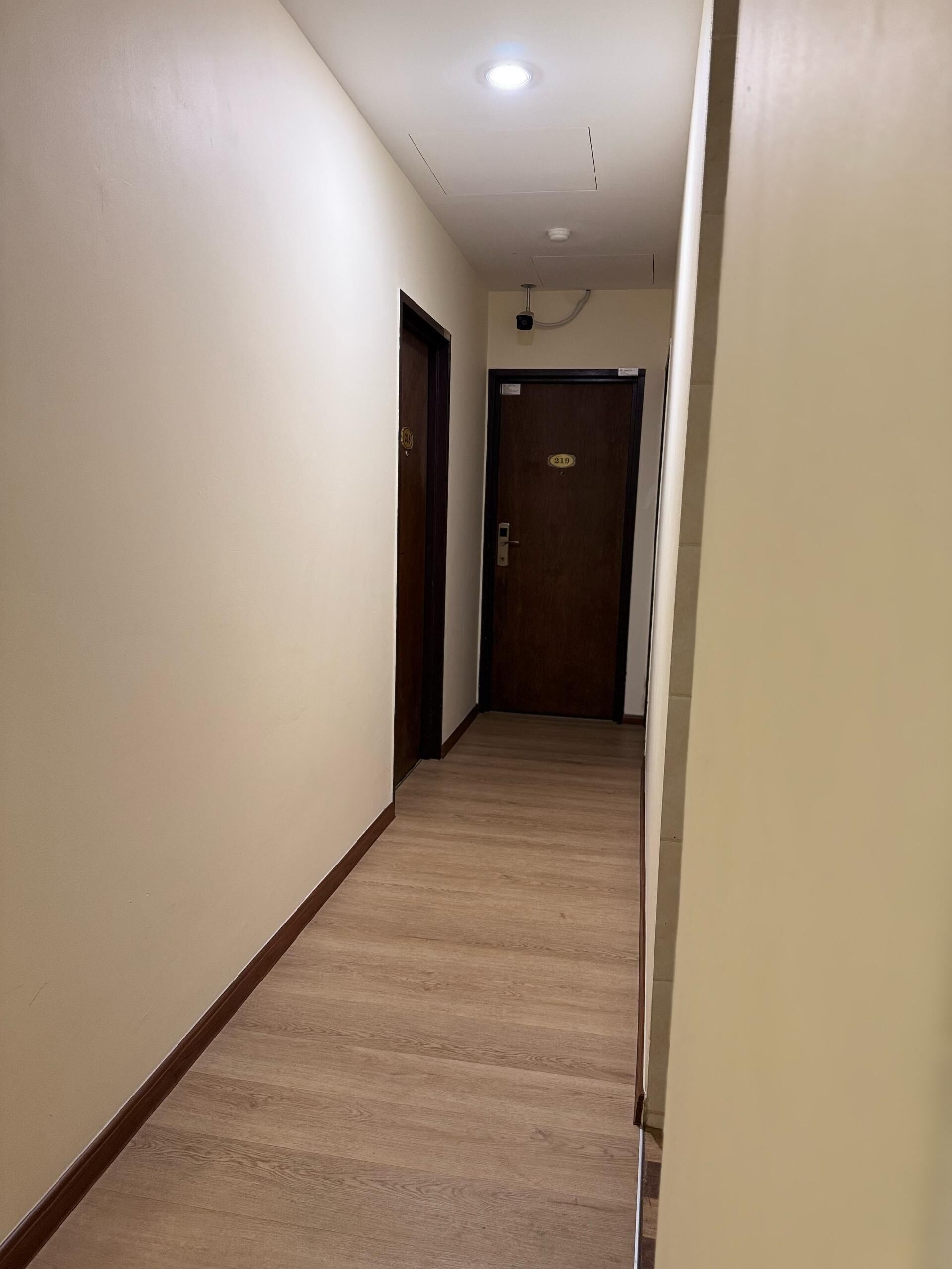A hallway with wooden flooring and white walls. There are two doors, one with a number plate.