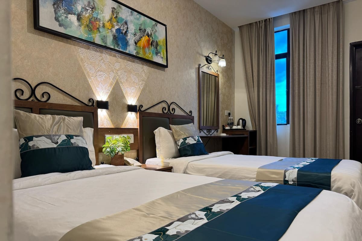 A hotel room with two beds, a large abstract painting, a mirror, and a window with curtains.