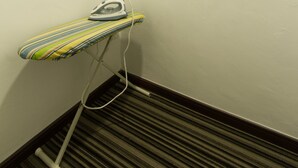A corner of a room with a striped floor, an ironing board with an iron, and a wall-mounted air conditioner. - JS Hotel (Johor Bahru)