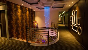 A hotel lobby with a spiral staircase, a decorative wall with a leaf pattern, and a modern light fixture. - JS Hotel (Johor Bahru)