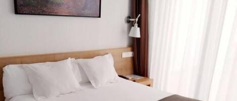 A hotel room with a large bed, a nightstand, a wall-mounted lamp, and a painting of a forest.