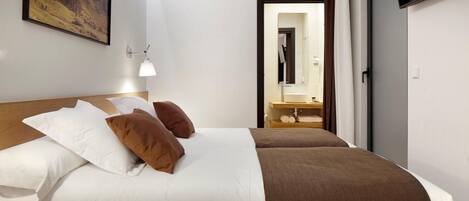 Une chambre d’hôtel avec un grand lit, une table de chevet, une télévision, un tableau au mur et une salle de bain visible à travers une porte ouverte.