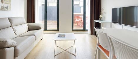A modern living room with a sofa, a small table, a TV, and a sliding glass door leading to an outdoor area with a chair.