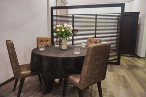 A round table with a dark tablecloth, surrounded by four upholstered chairs with a woven pattern. A vase with flowers is placed on the table. - Oliving Residence (Hanoi)