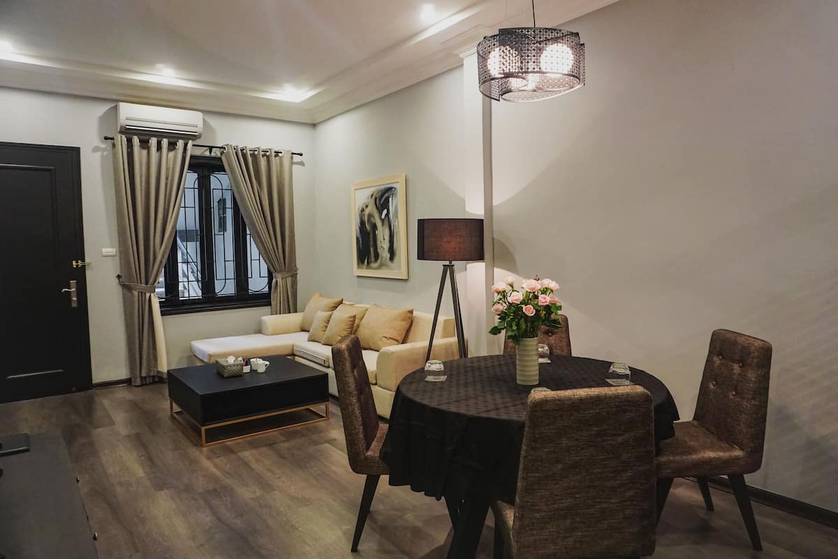 Ein modernes Wohnzimmer mit einer Couch, einem Esstisch und Stühlen. Es gibt ein Fenster mit Vorhängen, eine Lampe und ein Bild an der Wand.