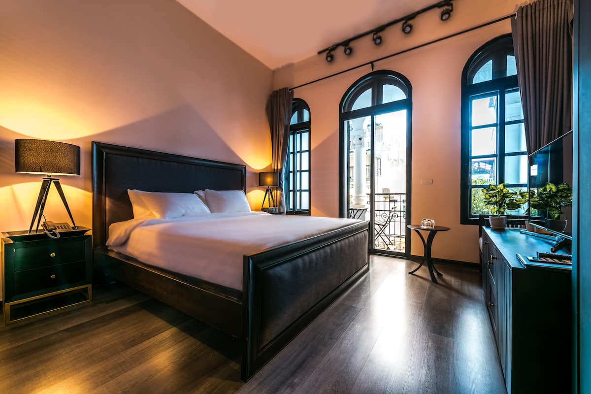 Ein modernes Hotelzimmer mit einem großen Bett, Nachttischen, einem kleinen Schreibtisch und einem Balkon mit Pflanzen.