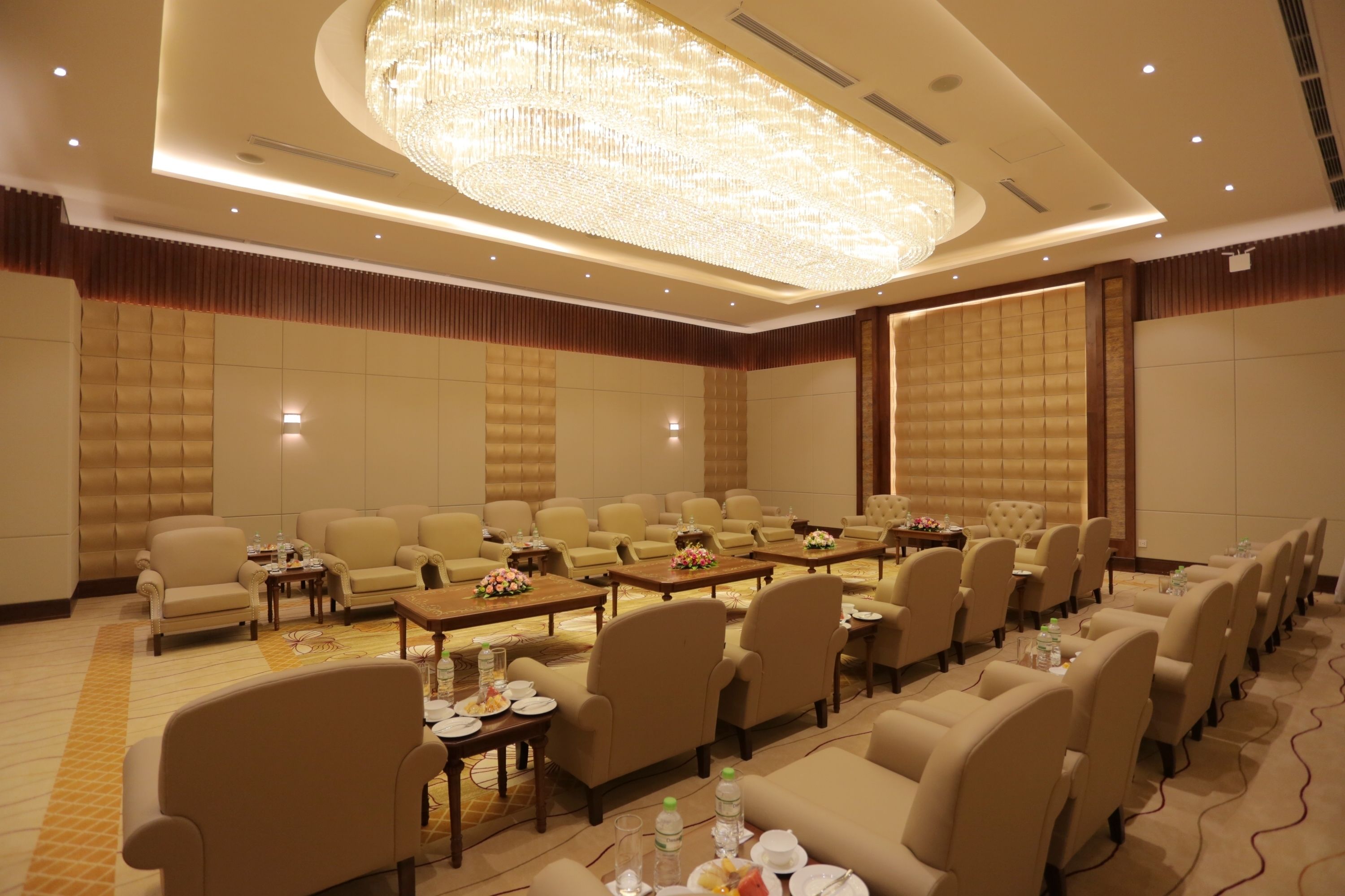 A conference room with rows of chairs, tables with floral centerpieces, and a large chandelier.
