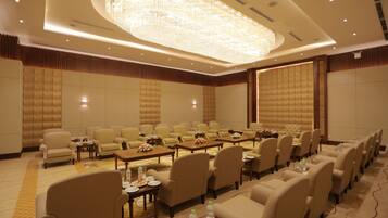 A conference room with rows of chairs, tables with floral centerpieces, and a large chandelier.