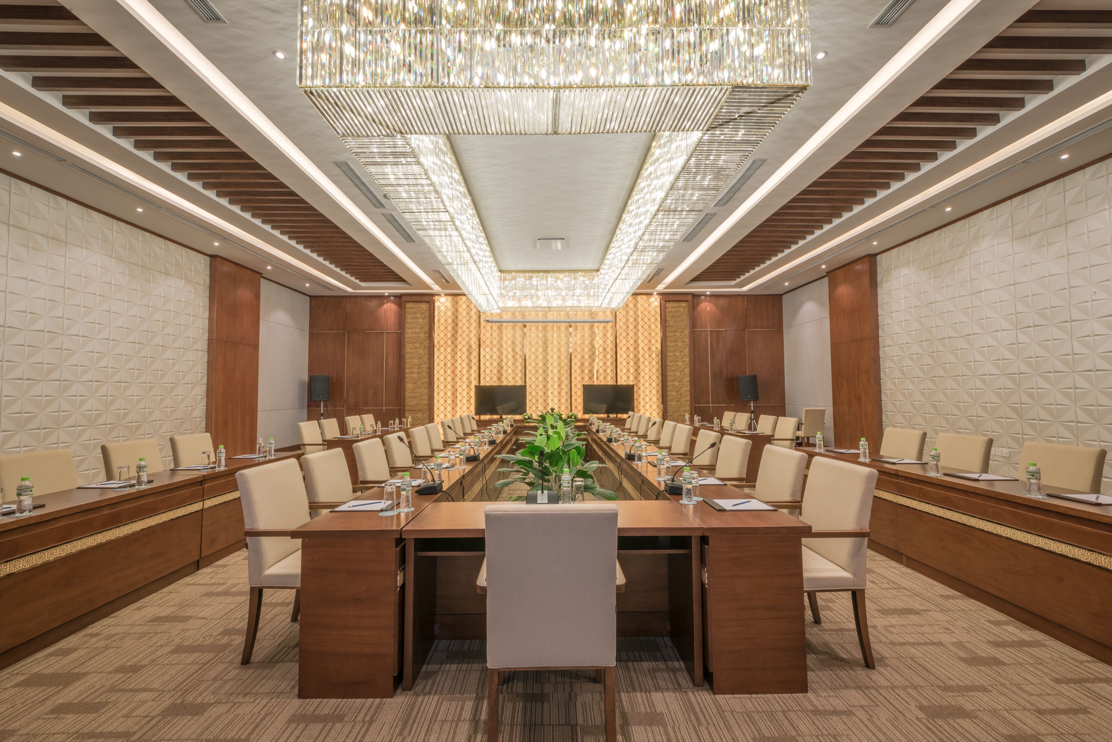 A conference room with a long table, chairs, a chandelier, and a patterned wall.