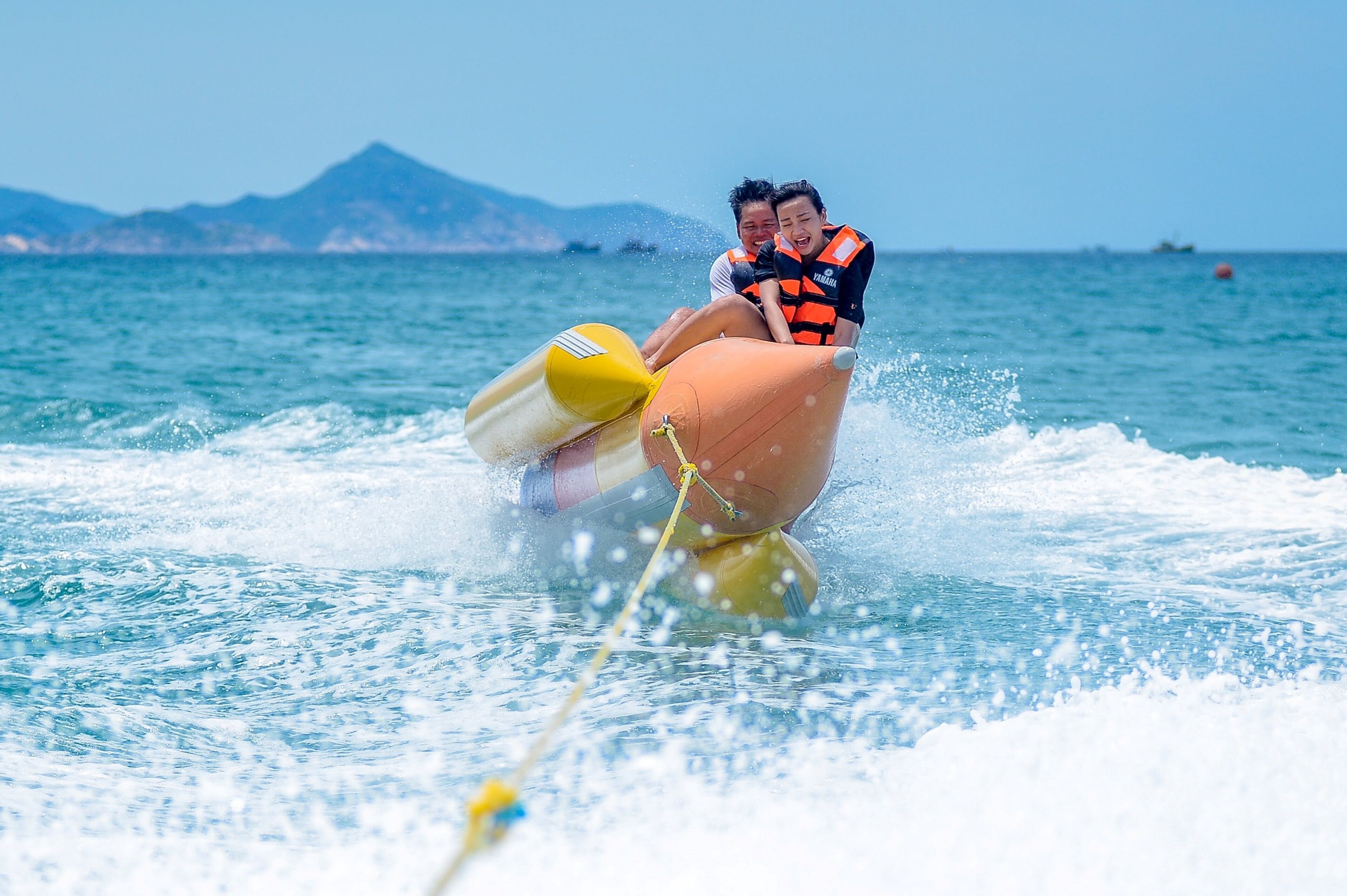 A person riding a jet ski with another person on board, in a body of water with mountains in the background.