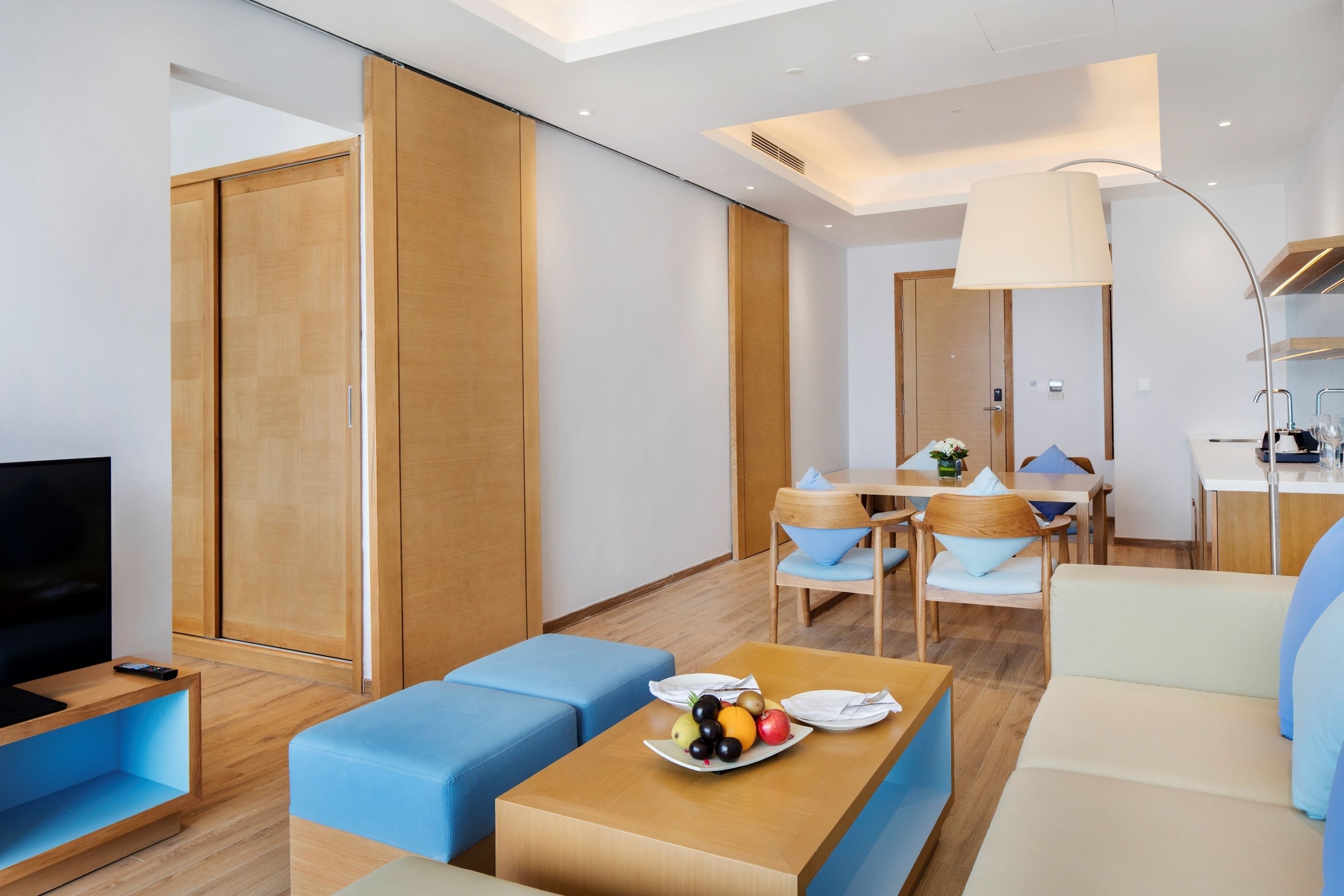 Une chambre d’hôtel moderne équipée d’une télévision, d’un canapé, d’une table à manger et d’une assiette de fruits.