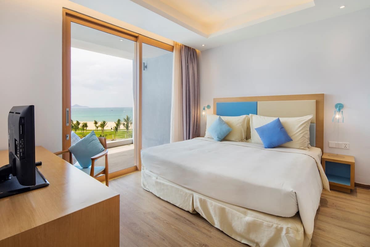 Habitación de hotel con una cama grande, televisor, escritorio y vista a la playa.