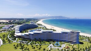 A large, modern hotel with multiple curved levels, a central pool, and a beachside location.