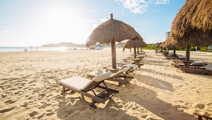 A beach with sun loungers and thatched umbrellas.