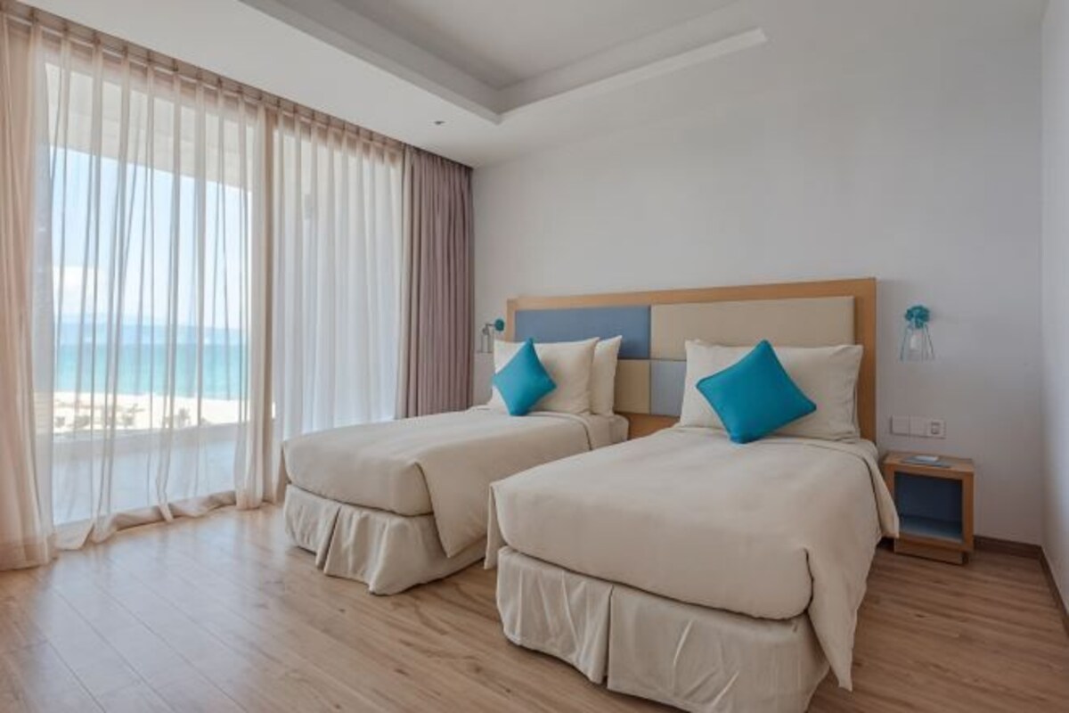 Een hotelkamer met twee bedden, een nachtkastje en uitzicht op het strand.