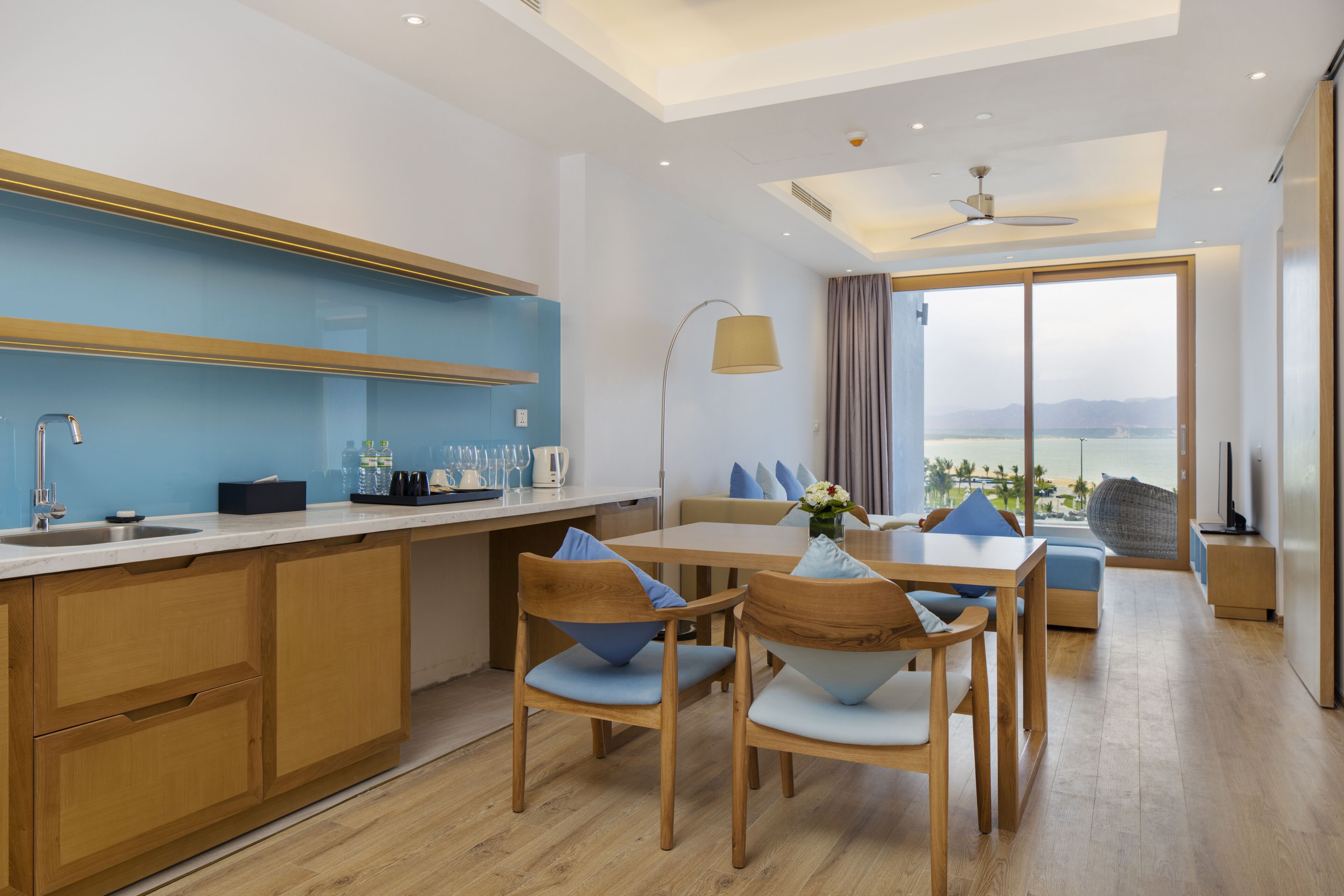 Une cuisine moderne avec des meubles en bois, un coin repas comprenant une table et des chaises, et une grande fenêtre offrant une vue sur la mer.