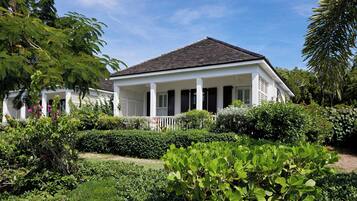 A white colonial-style house with a dark roof, surrounded by lush greenery and a well-maintained garden.