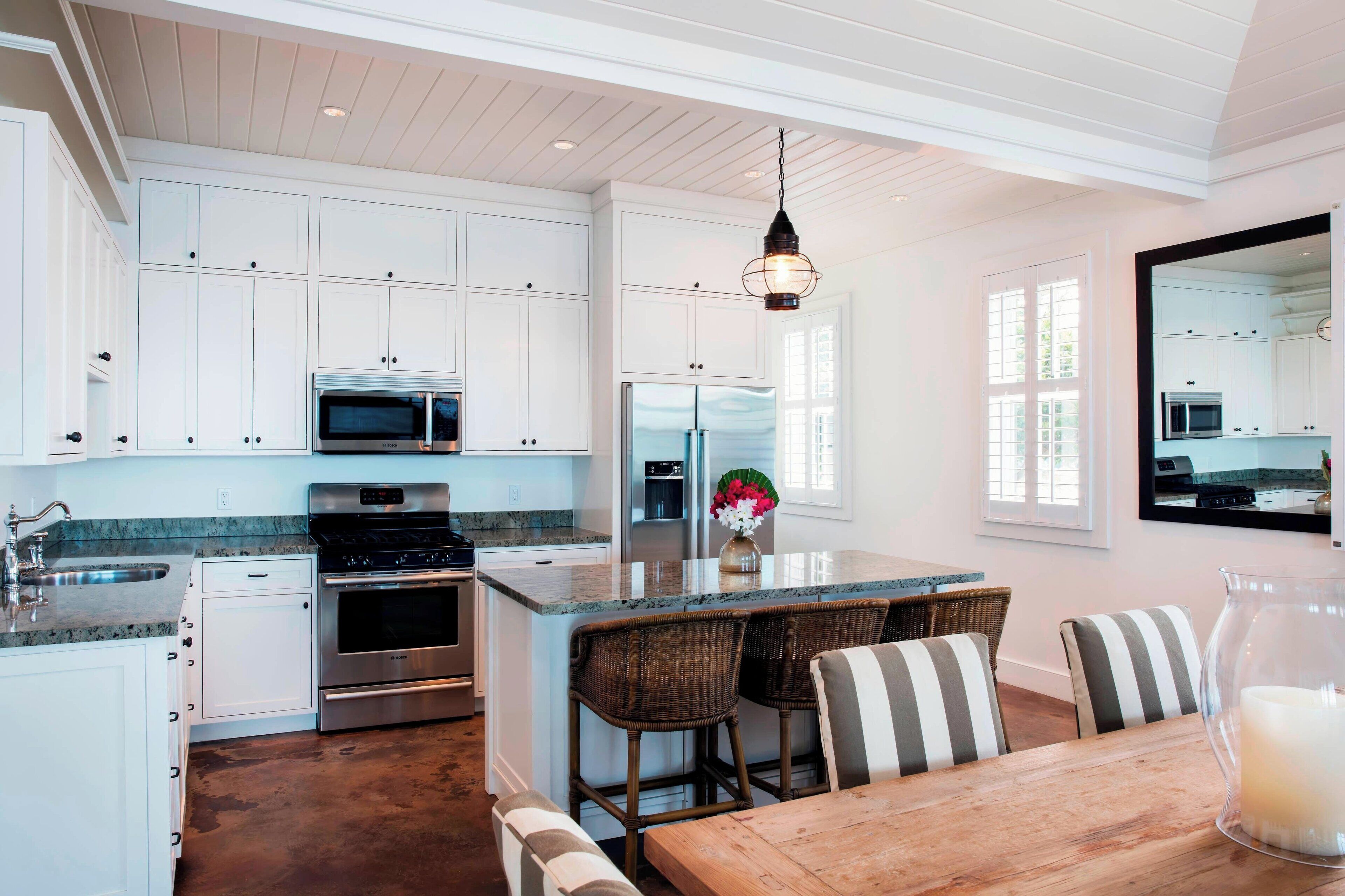 A modern kitchen with white cabinetry, stainless steel appliances, a wooden dining table, and a large island with bar stools.