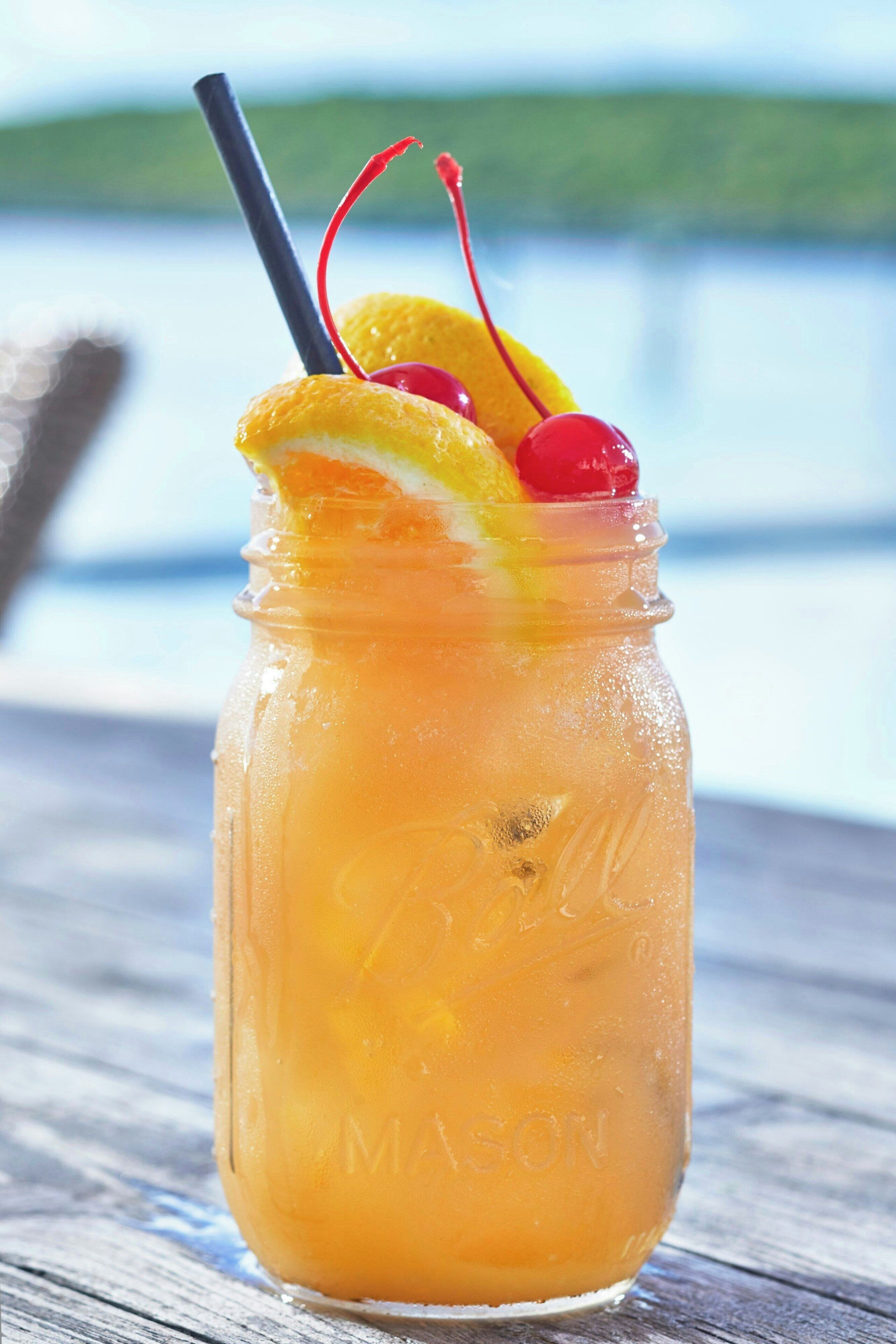 A mason jar with a straw and fruit garnish on a wooden surface.