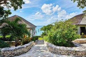 Un sendero conduce a una zona de piscina con muros de piedra y plantas tropicales.