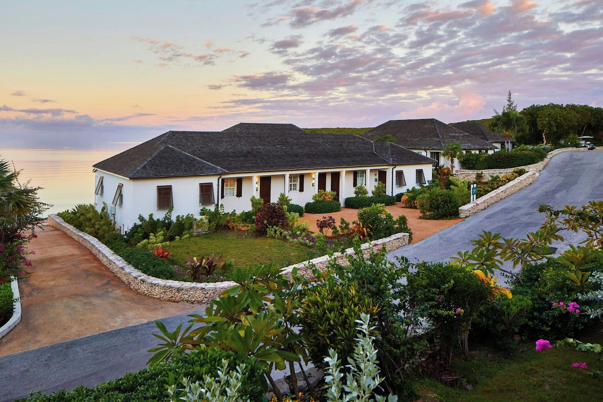 A coastal property with a white building, a paved driveway, and lush greenery.