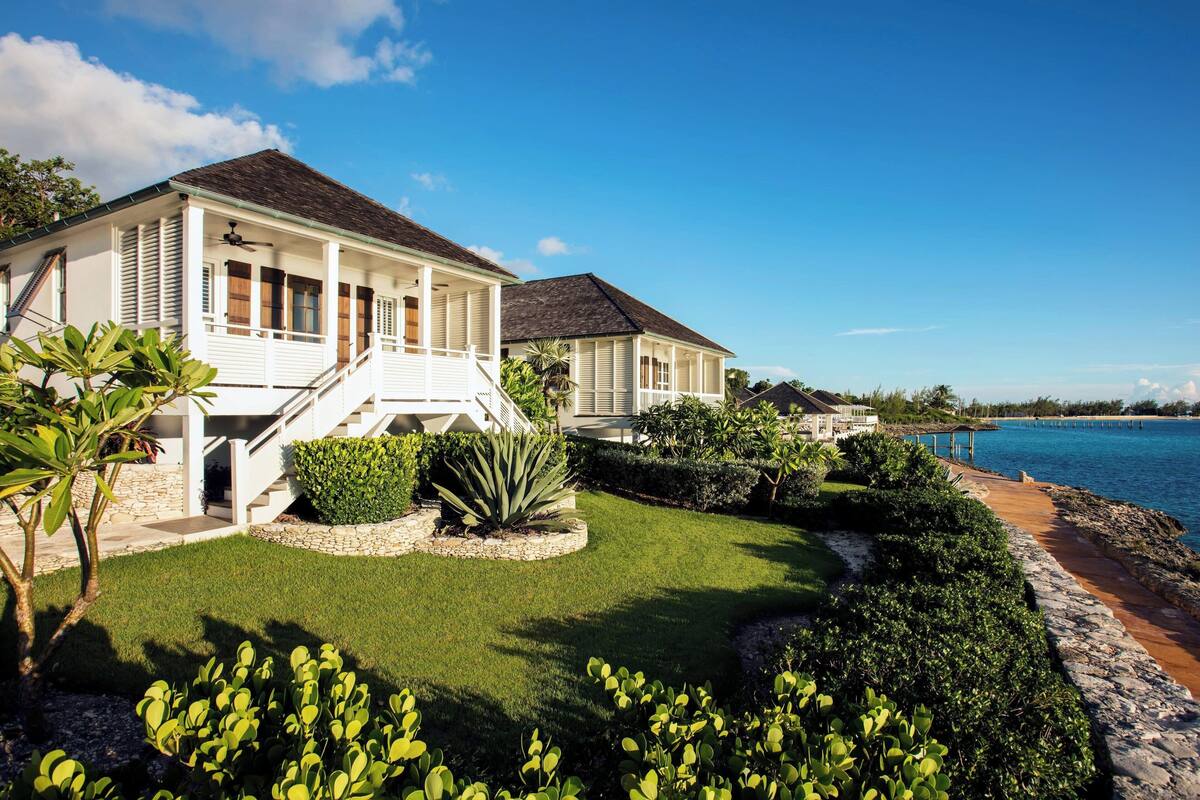 A beachfront property with a large house, a covered porch, and a well-maintained lawn.