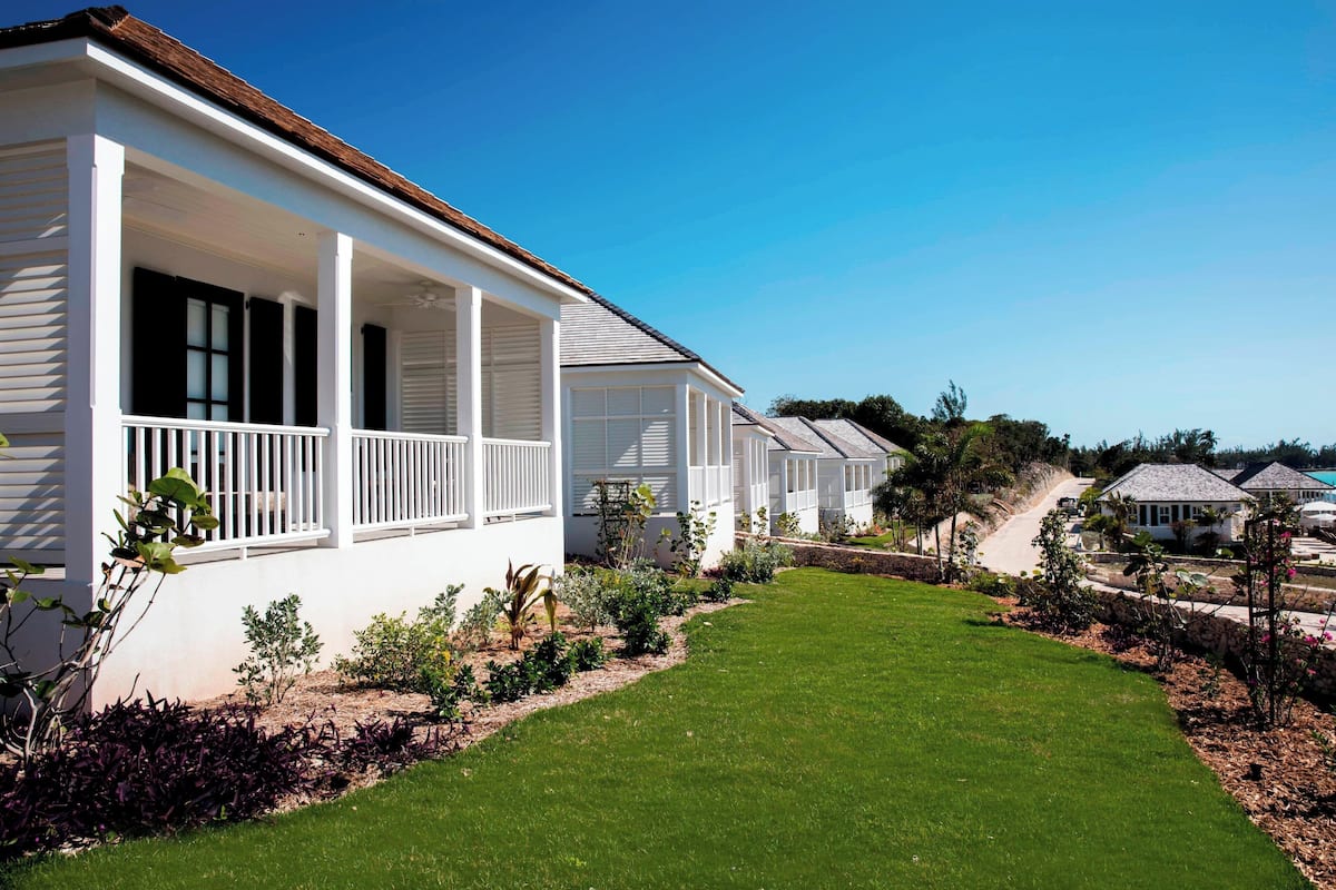 A row of white houses with white railings, a well-maintained lawn, and a clear blue sky.