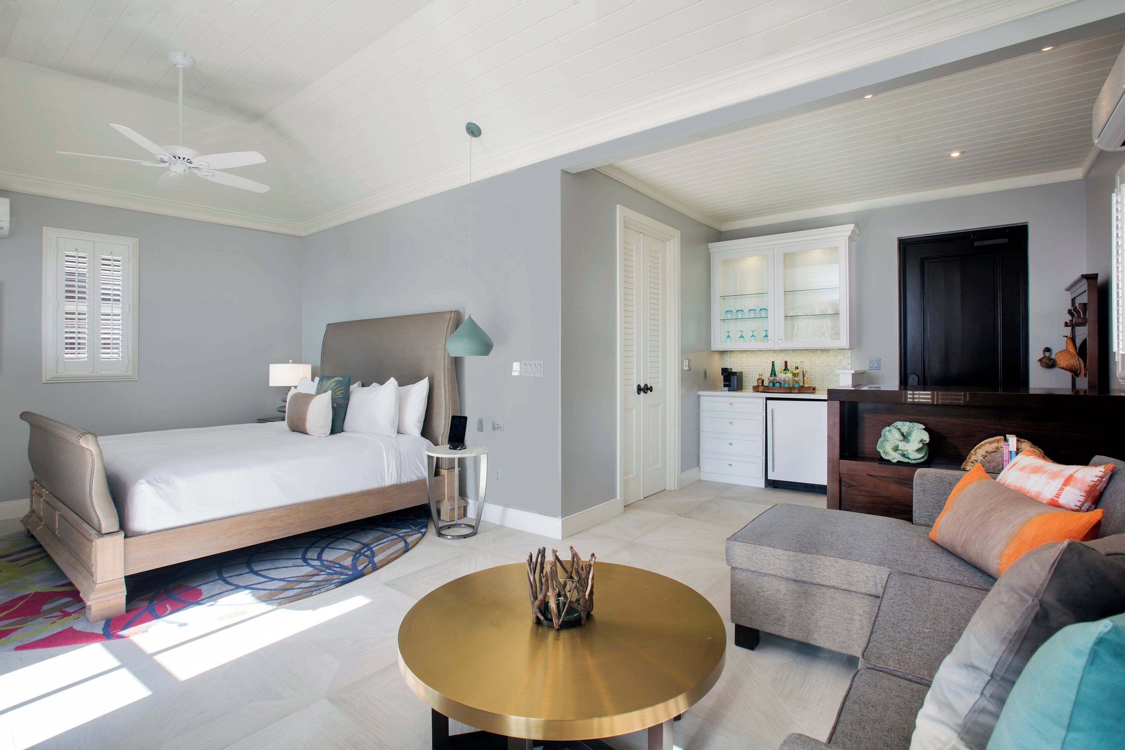 Un dormitorio moderno con cama, mesita de noche y lámpara. Hay una zona de comedor con mesa y sillas, y una cocina con armarios y refrigerador.