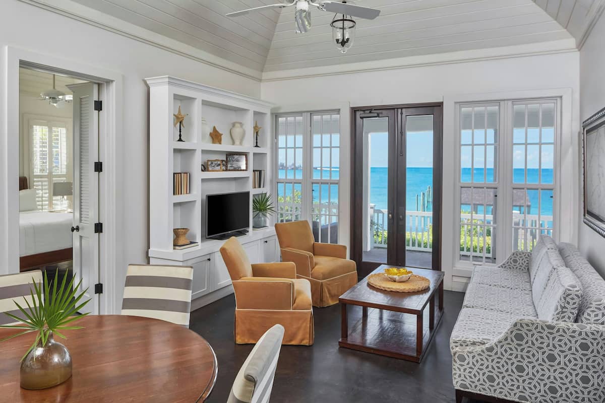 A spacious living room with a large window offering a view of the ocean, a white entertainment unit, and comfortable seating.