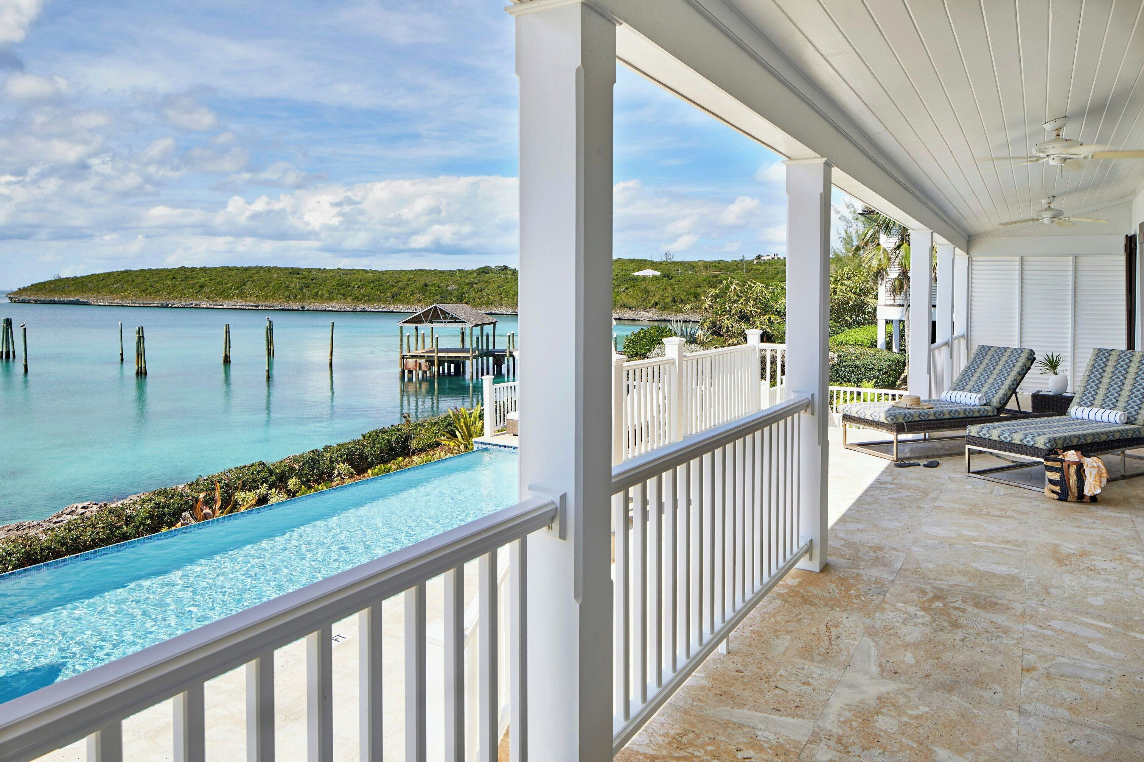 A covered outdoor area with a pool, lounge chairs, and a view of the sea.