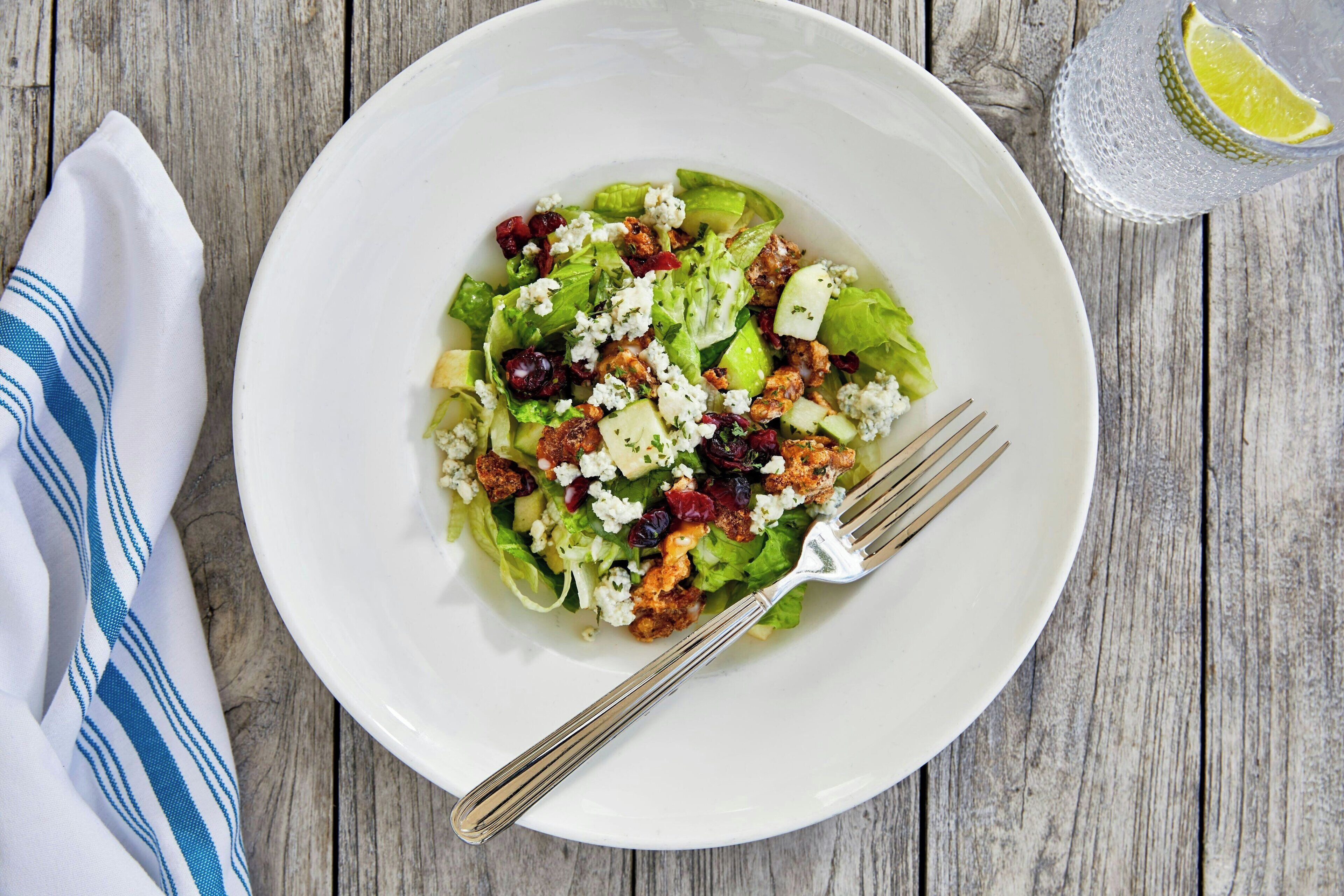 Une assiette blanche avec une salade, posée sur une table en bois.