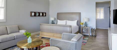 A bedroom with a bed, a sofa, a chair, a small table, and a TV.