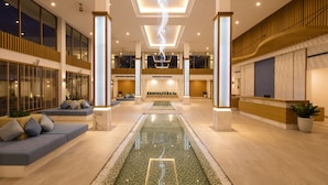 Un hall d’entrée spacieux agrémenté d’un élément décoratif central avec de l’eau, de coins salon et un comptoir d’accueil.