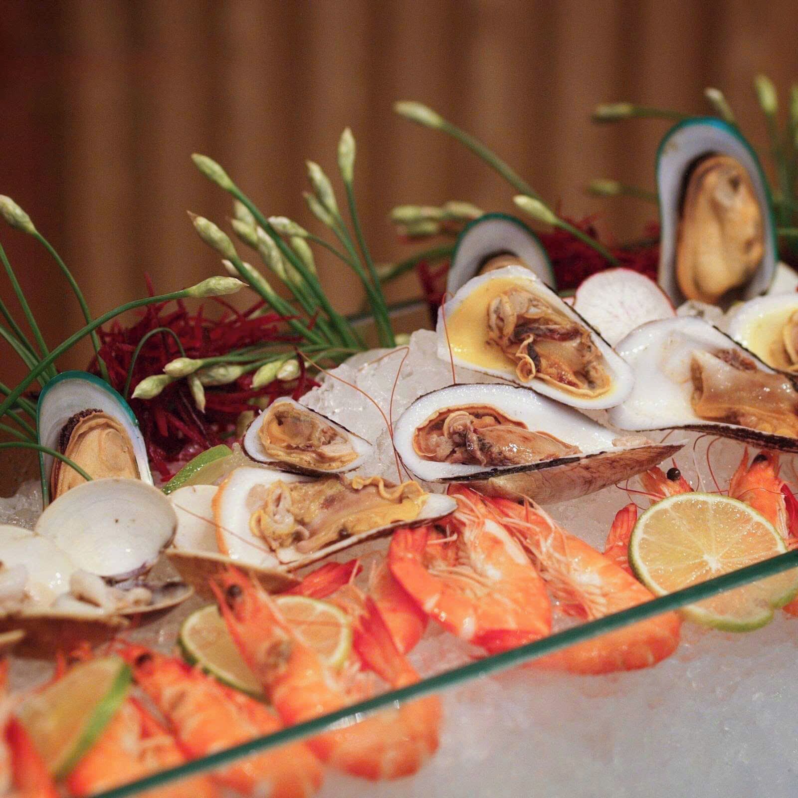 Una bandeja de mariscos con ostras, camarones y rodajas de limón sobre hielo.