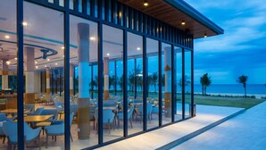 Un espace de restauration extérieur moderne, doté de murs en verre, de tables et de chaises, et offrant une vue sur la plage.