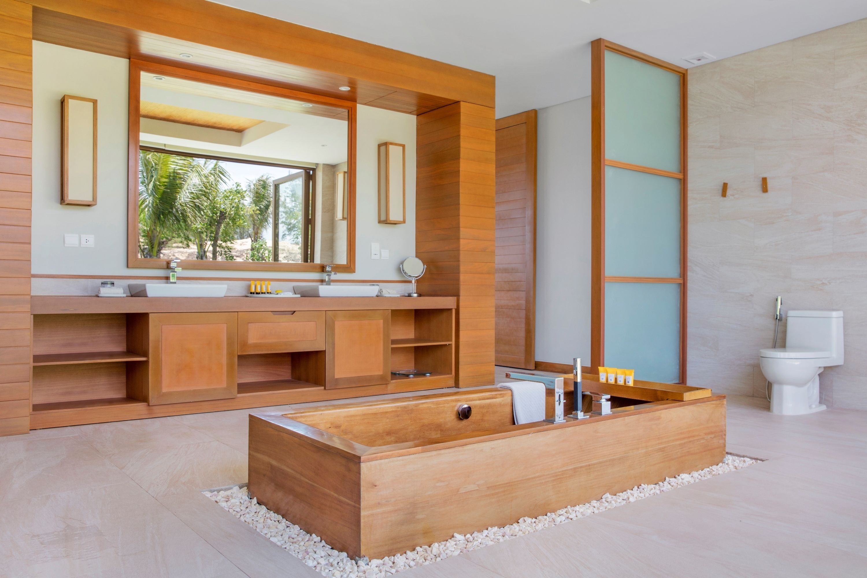 A modern bathroom with a wooden vanity, a large mirror, a freestanding bathtub, and a toilet.